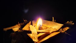 Detail: kleine Flamme entzündet Holzspäne im Dunkeln
