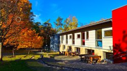 Außenansicht eines Schullandheims bei Herbstsonne; bunte Bäume und Sitzbänke.