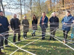 Teilnehmende halten im Freien ein Netz aus Seilen bei einer Teamübung.